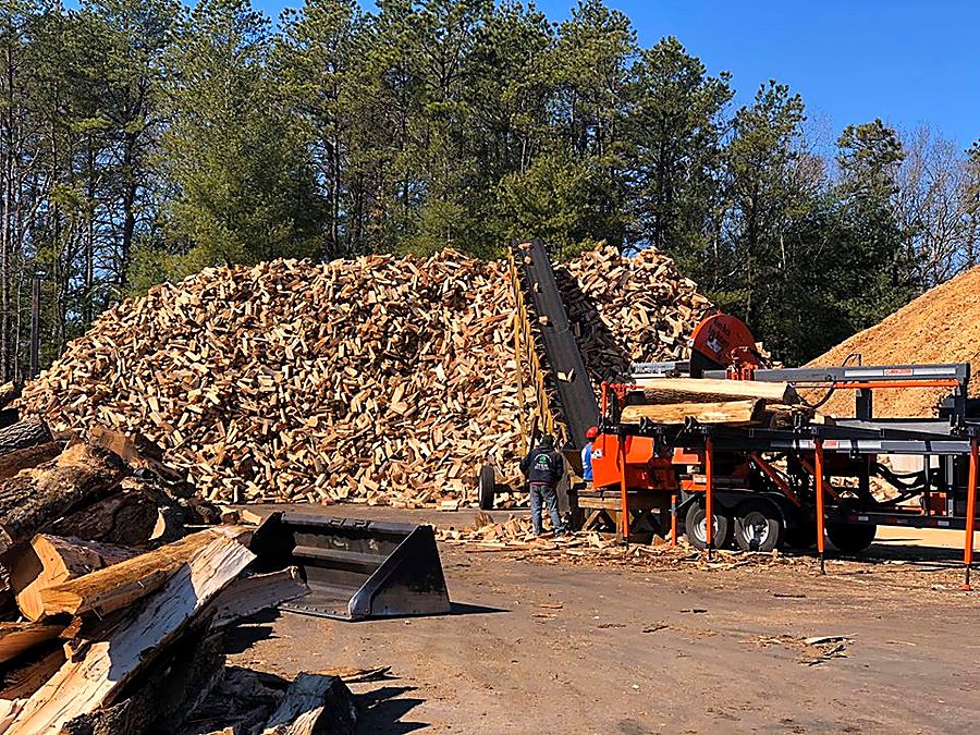 Split firewood and mulch stockpiled at the Mulch N' More yard, with the processor and loader working alongside