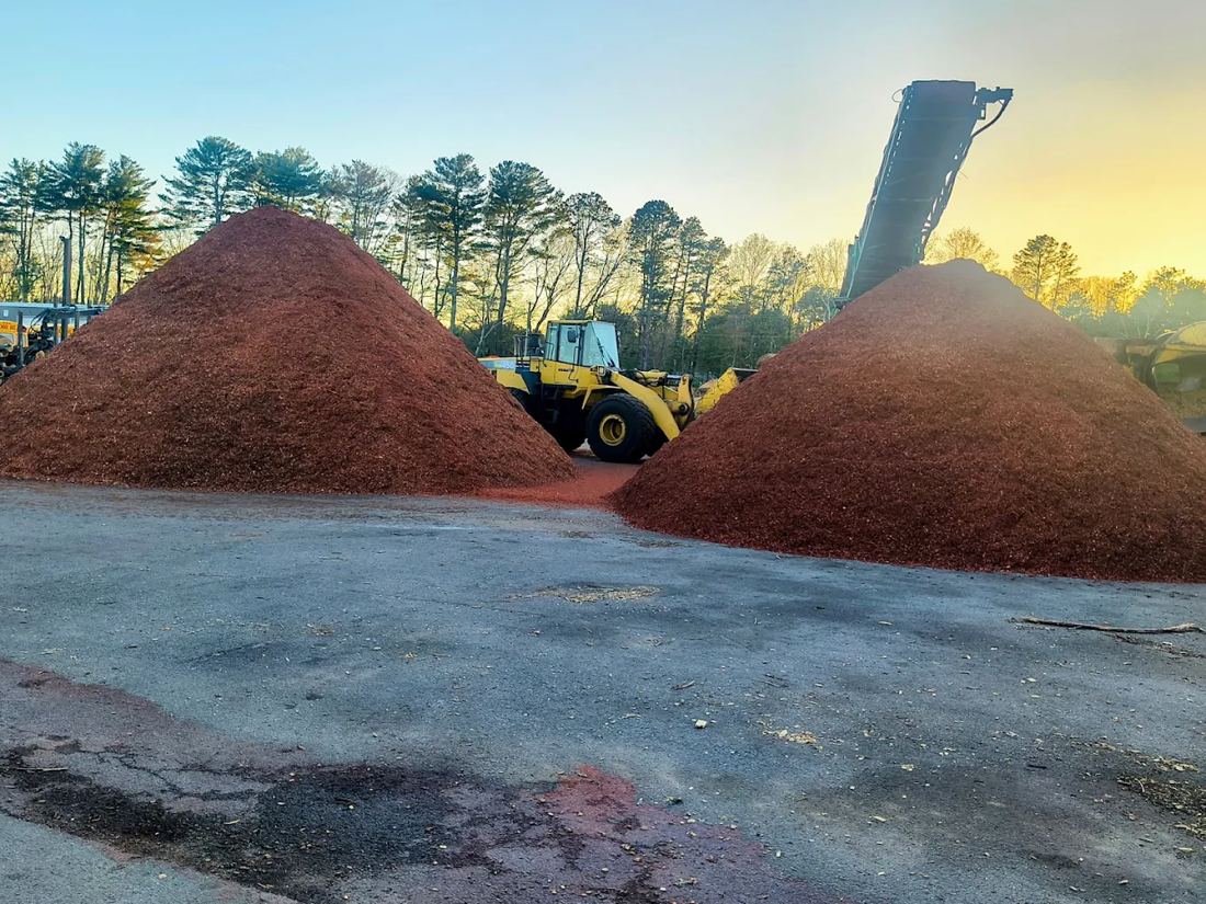 Loader between two piles of red mulch at the Mulch N' More yard in Exeter, Rhode Island, at sunset