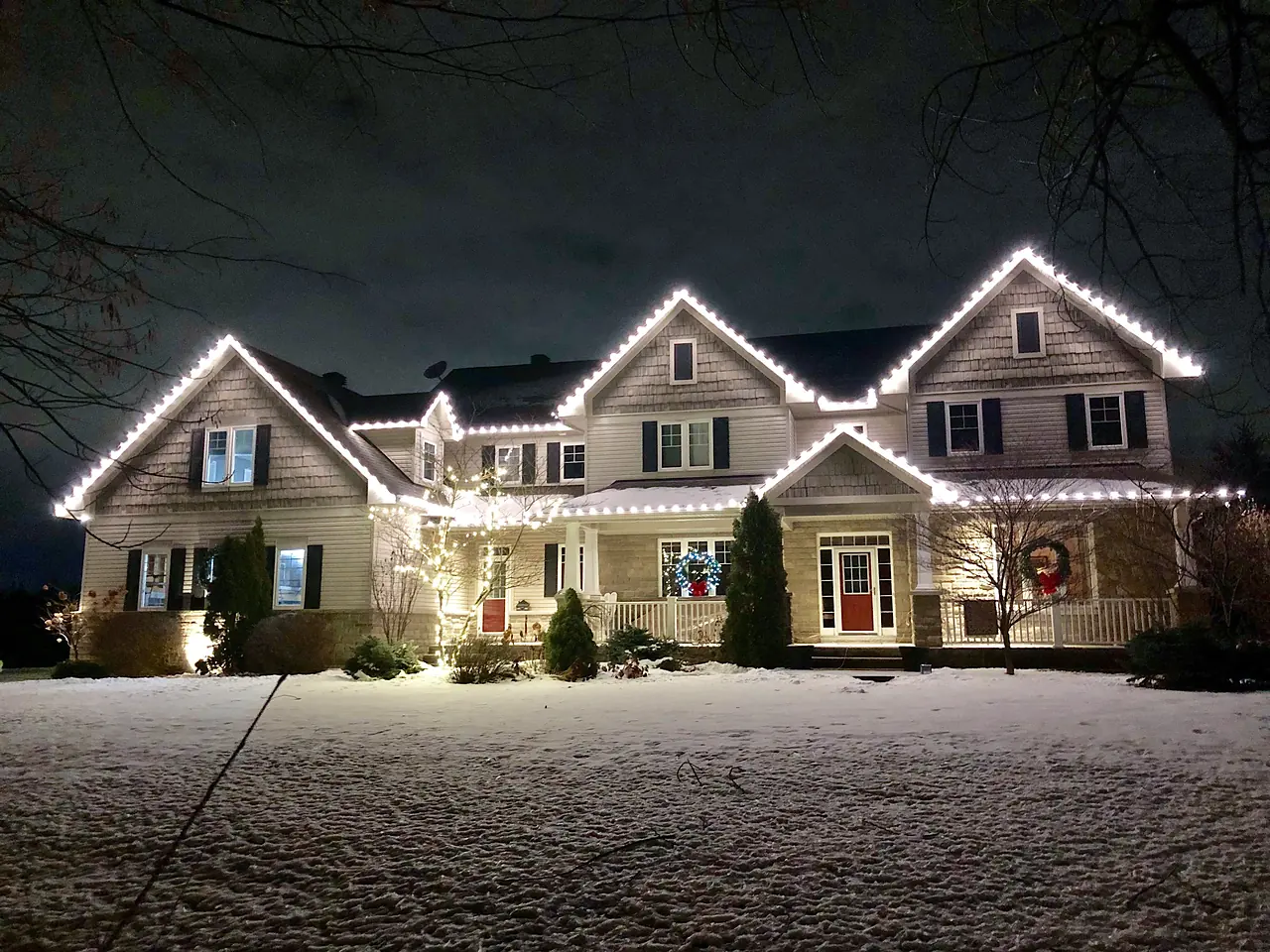 Two-story home with white holiday lights along the rooflines on a snowy night