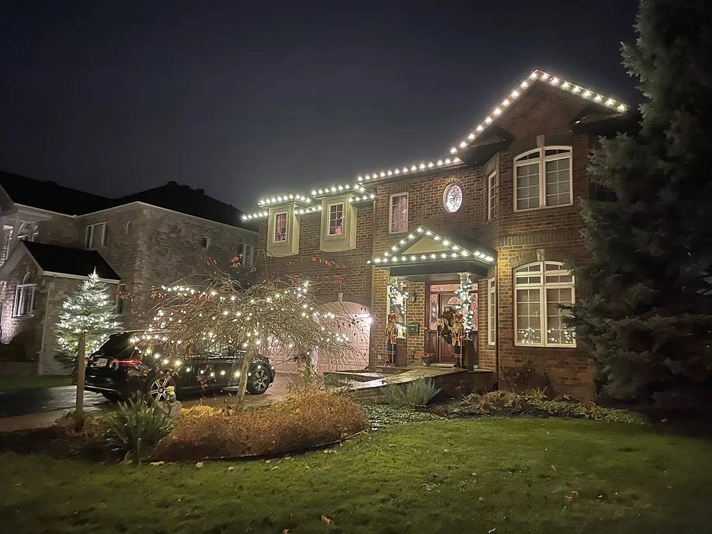 Brick home with white roofline lights, a lit porch and a lit front-yard tree