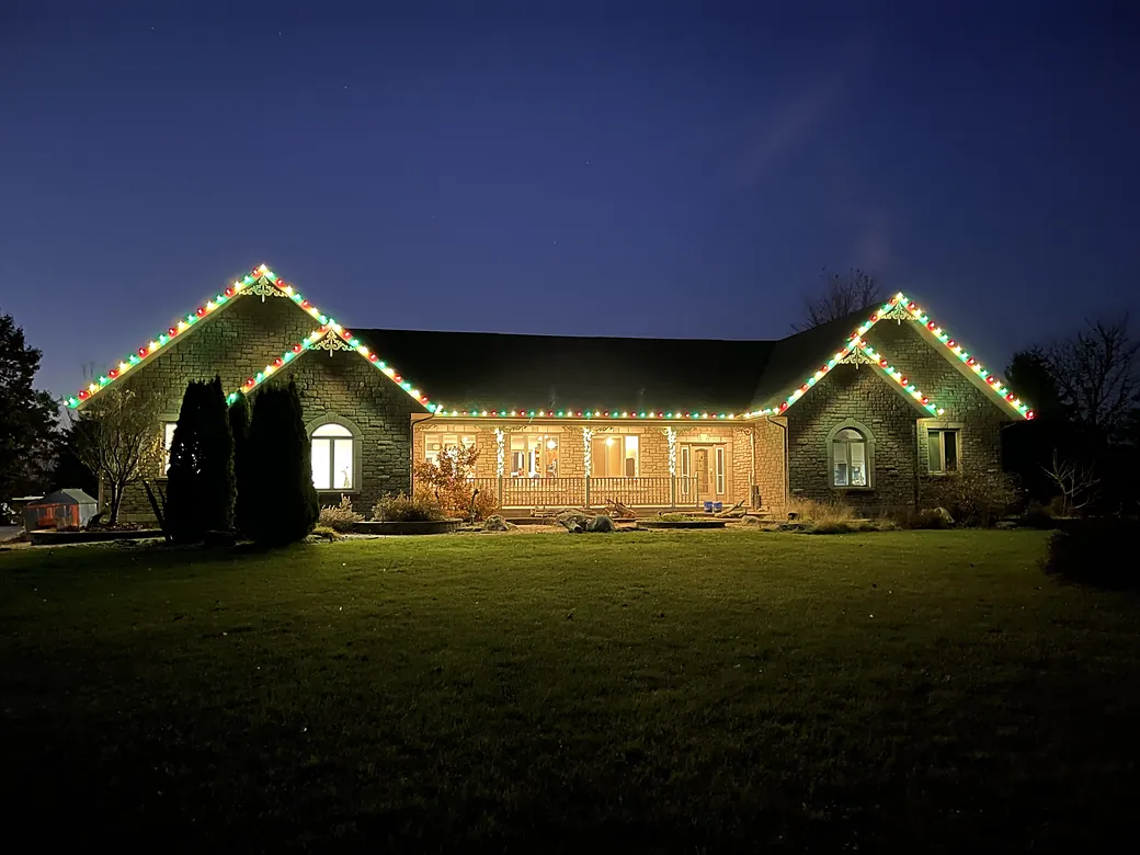 Ranch home with multicolor holiday lights along the rooflines at dusk